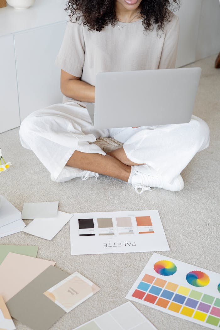 Young woman reviews color palettes for design project on laptop, sitting indoors.
