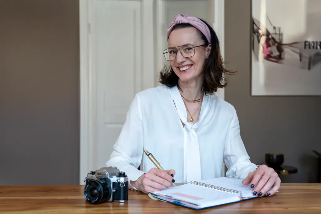 Brandingfotografie Businessfotografie Antje Weißmann Fotografin Frau am Schreibtisch, Kamera und Schreibblock liegen vor ihr auf dem Tisch, Stift in der Hand
